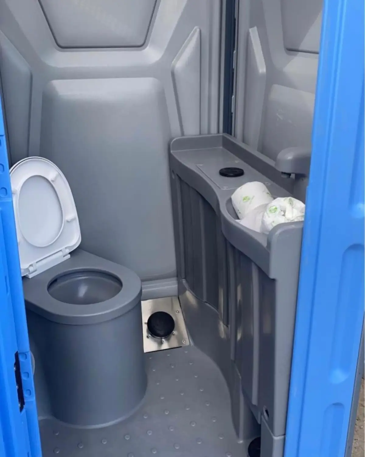 Interior of a porta potty with a toilet seat and a small shelf