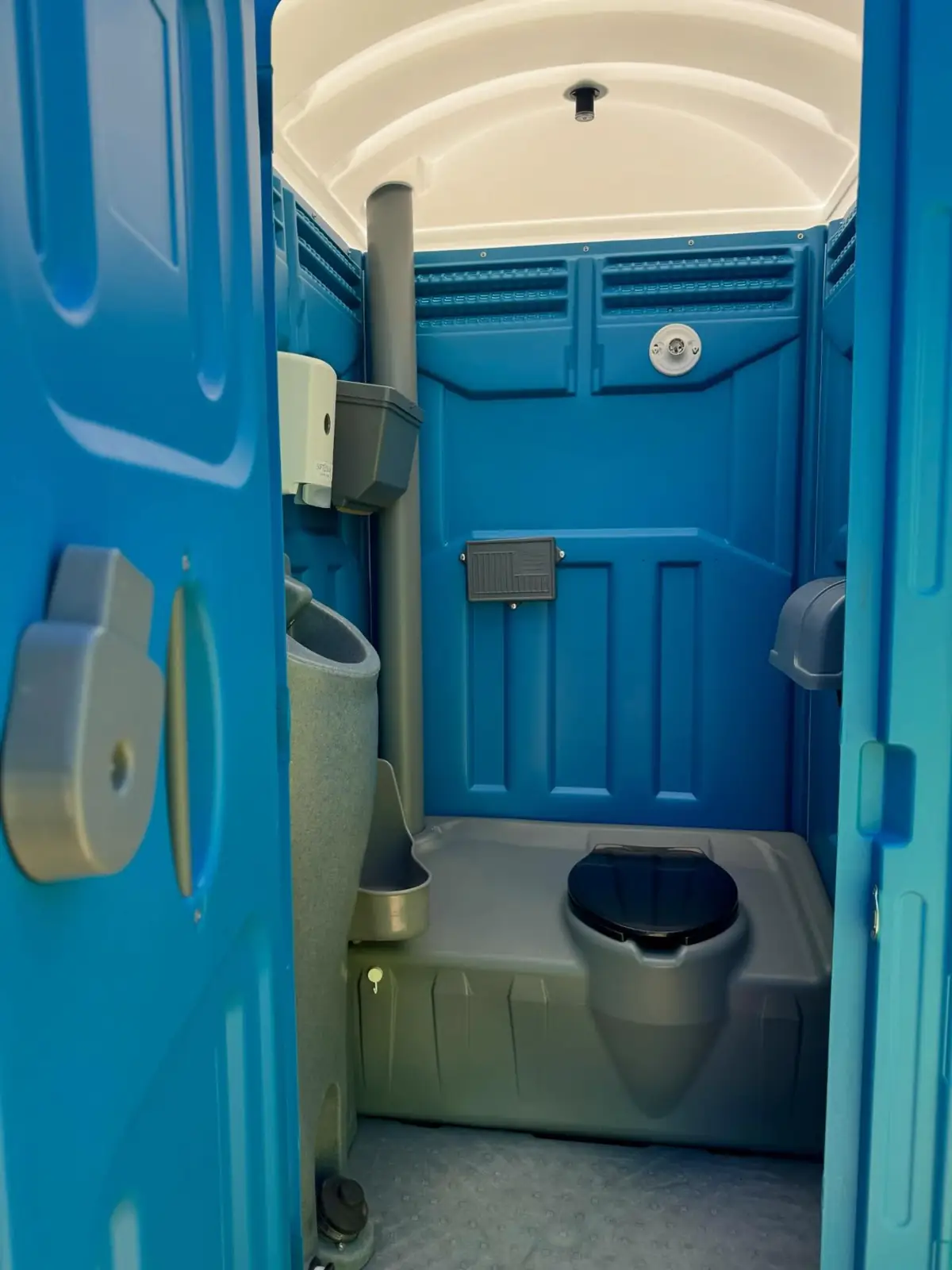 Inside a blue flushing porta potty showing the flush tank and hand sanitizer