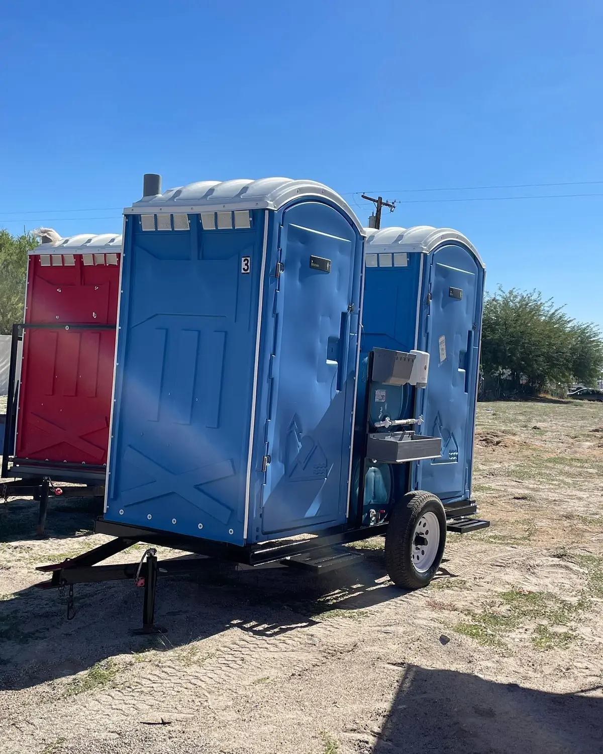 Blue standard porta potties strapped upright on a flatbed delivery trailer