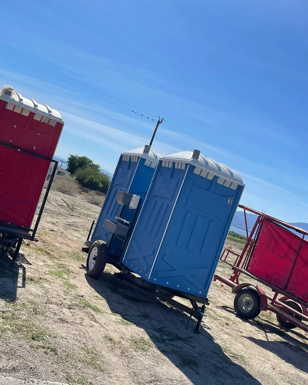 Porta potties strapped on a delivery trailer parked at a dirt construction site