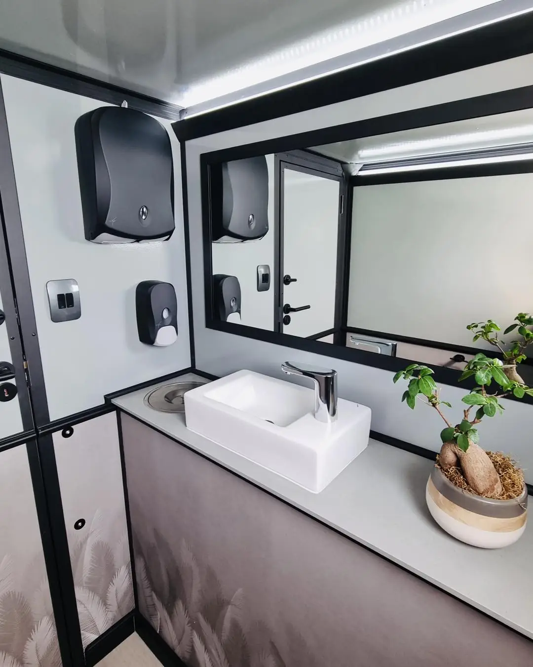 Restroom trailer interior with a vessel sink, mirror and soap and towel dispensers