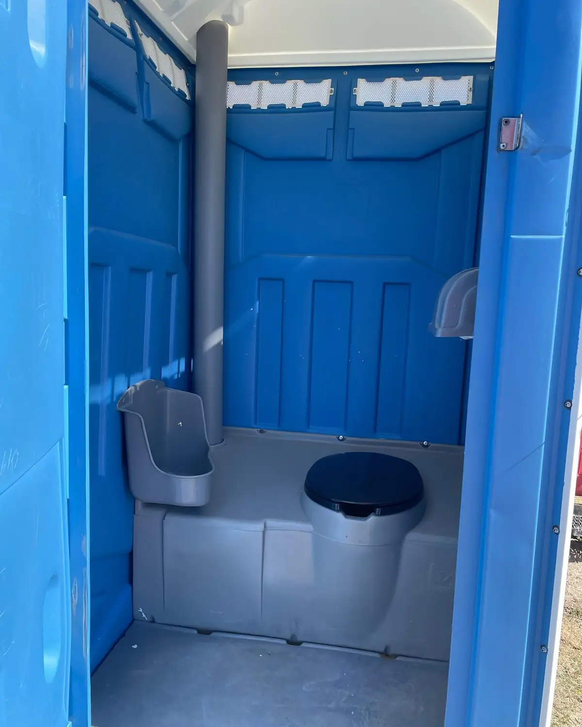 Inside a blue standard porta potty with urinal, toilet seat and two toilet paper rolls