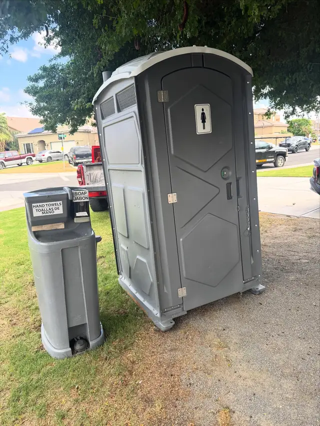 Gray porta potty beside a foot-pump handwashing station