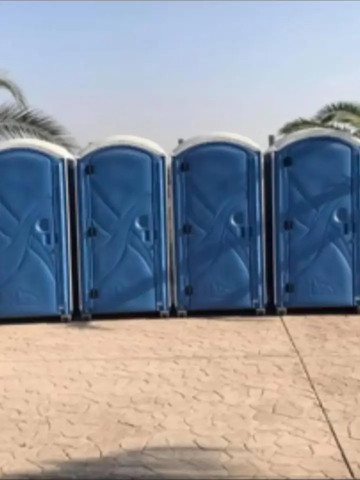 Four blue porta potties in a row on a driveway
